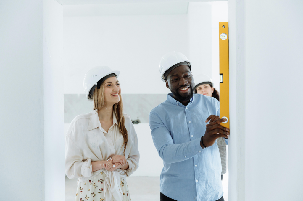 Two people wearing construction hats measuring a wall with a level.